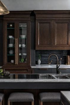 a kitchen with dark wood cabinets and marble counter tops, along with stools in front of the sink