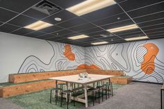 an empty conference room with benches and tables in front of a mural on the wall