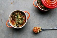 two red pots filled with food next to spoons on top of a cement surface