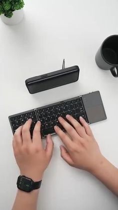 a person is typing on a keyboard at a desk with other office supplies and plants