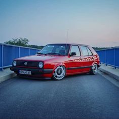 a red car parked on the side of a road next to a blue wall and fence