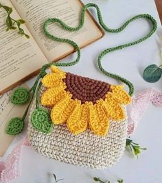 a crocheted sunflower purse sitting on top of a table next to an open book