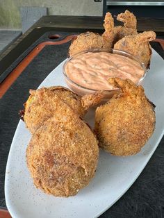 some fried food on a white plate with a dipping sauce in the middle and other foods around it