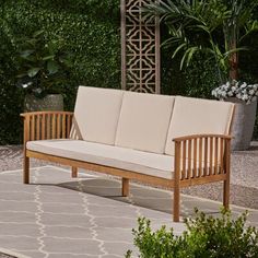 a wooden bench sitting on top of a rug in front of a tree and shrubbery