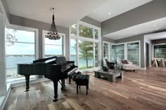 a living room filled with furniture and a grand piano in front of large windows overlooking the water