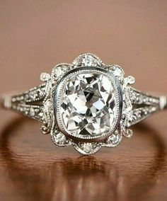 an antique style engagement ring with a center stone surrounded by diamonds on a wooden surface