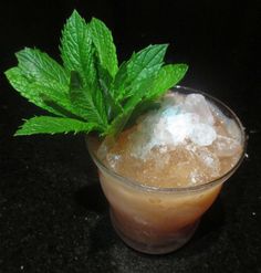 a small glass filled with ice and mint on top of a black counter next to a green leaf