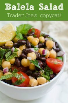 a white bowl filled with black beans, tomatoes and lettuce next to a lemon wedge