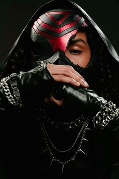 a woman wearing a red and black mask with chains on her hands, holding onto the hood