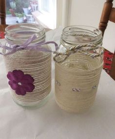 two mason jars with purple flowers and twine are sitting on a white tablecloth