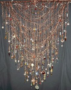 a piece of art made out of beads and chains hanging on a wall with a curtain behind it