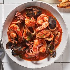 a white bowl filled with shrimp and mussels on top of a tiled floor