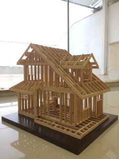 a wooden model of a house sitting on top of a white floor next to a window