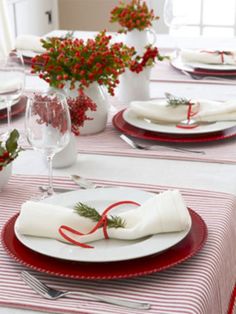 the table is set for christmas dinner with red and white plates, napkins, and flowers