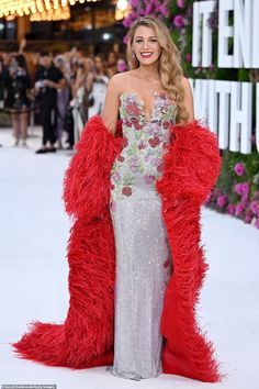 a woman in a red and silver dress standing on a white carpet with flowers around her