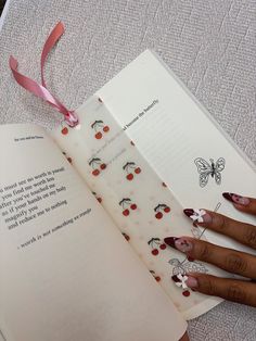 a woman's hands holding an open book with cherry decorations on it and pink ribbon