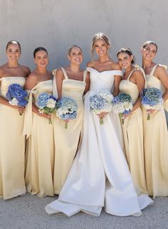 a group of women standing next to each other wearing dresses and holding bouquets in their hands