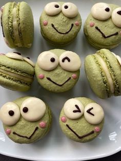 some green macaroons with white frosting and faces drawn on them are sitting on a plate