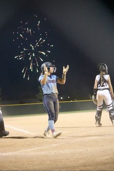 a softball player holding her hand up in the air as fireworks go off behind her