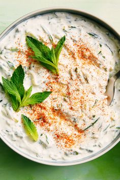 a bowl filled with white sauce and topped with green leaves on the side next to a spoon