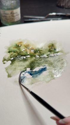 a person is holding a paintbrush and drawing on paper with watercolors in front of them