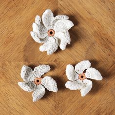 three white crocheted flowers sitting on top of a wooden table next to each other