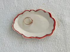 a white and red dish with a gold ring on the bottom, sitting on a table cloth