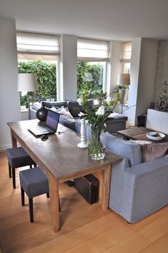 a living room filled with furniture and a wooden table in front of two large windows