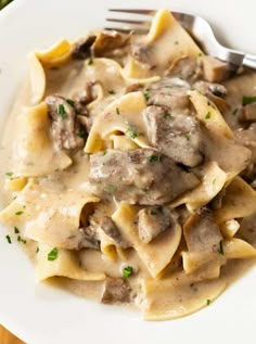 a white plate topped with pasta covered in meat and gravy next to a fork