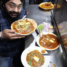 a man holding two plates of food in front of other dishes on the counter top