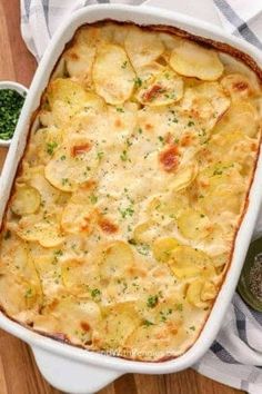 a casserole dish with potatoes in it on a wooden table next to a spoon