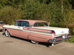 an old pink and white car is parked on the side of the road