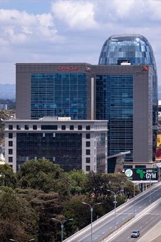 a large building on the side of a highway with cars driving by it and tall buildings in the background