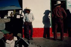 two men standing in front of a building with their shadows on the wall and one man wearing a cowboy hat