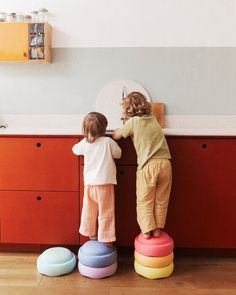 two young children standing on stools in front of a kitchen counter with colorful balls