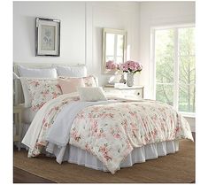 a white bed with pink flowers on it in a bedroom next to a window and dresser