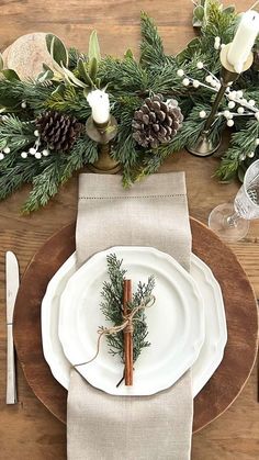 a place setting with pine cones, greenery and napkins on a wooden table