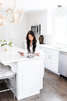 a woman sitting at a white kitchen island with flowers on the counter and magazines in front of her