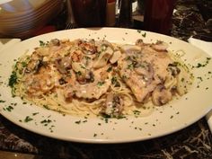 a white plate topped with pasta covered in mushroom sauce and parsley on top of a marble table