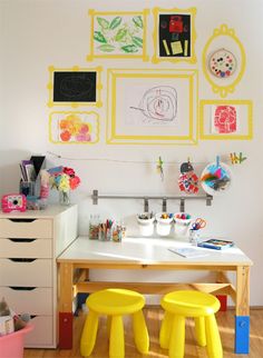 a child's desk with yellow stools and pictures on the wall above it