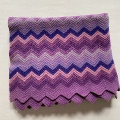 a purple and blue knitted blanket sitting on top of a white table next to a wall