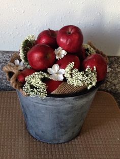 a bucket filled with red apples sitting on top of a table next to a wall