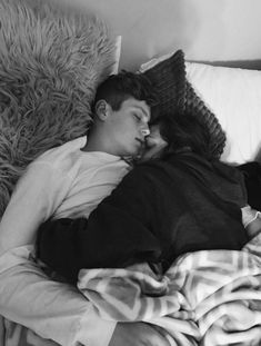 a man and woman sleeping on a bed next to each other in black and white