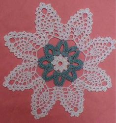 crocheted doily on pink background with white and green flowers in the center