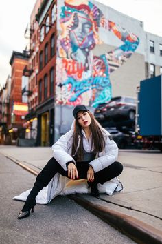 a woman sitting on the ground in front of a building with graffiti painted on it