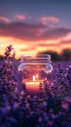 a jar with a lit candle in it surrounded by lavender flowers at sunset or dawn