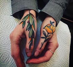 two people with tattoos on their hands holding each other's fingers, one has an orange and the other has green leaves