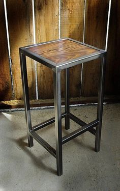 a metal and wood side table sitting in front of a wooden paneled wall,