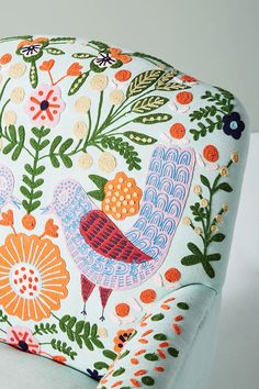 an upholstered seat cushion with colorful birds and flowers on the back, sitting on a white surface