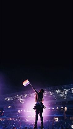 a woman holding up a flag in front of a large crowd at a concert or show